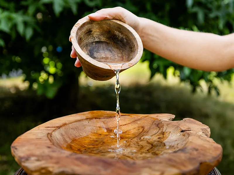 De houten doopschaal staat in de natuur Een hand giet water uit een houten kom in de doopschaal.